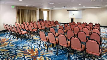 Una sala de conferencias con filas de sillas anaranjadas, una pantalla de proyector y un atril.