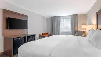 A hotel room with a large bed, a flat-screen TV mounted on the wall, a desk with a microwave, and a chair.
