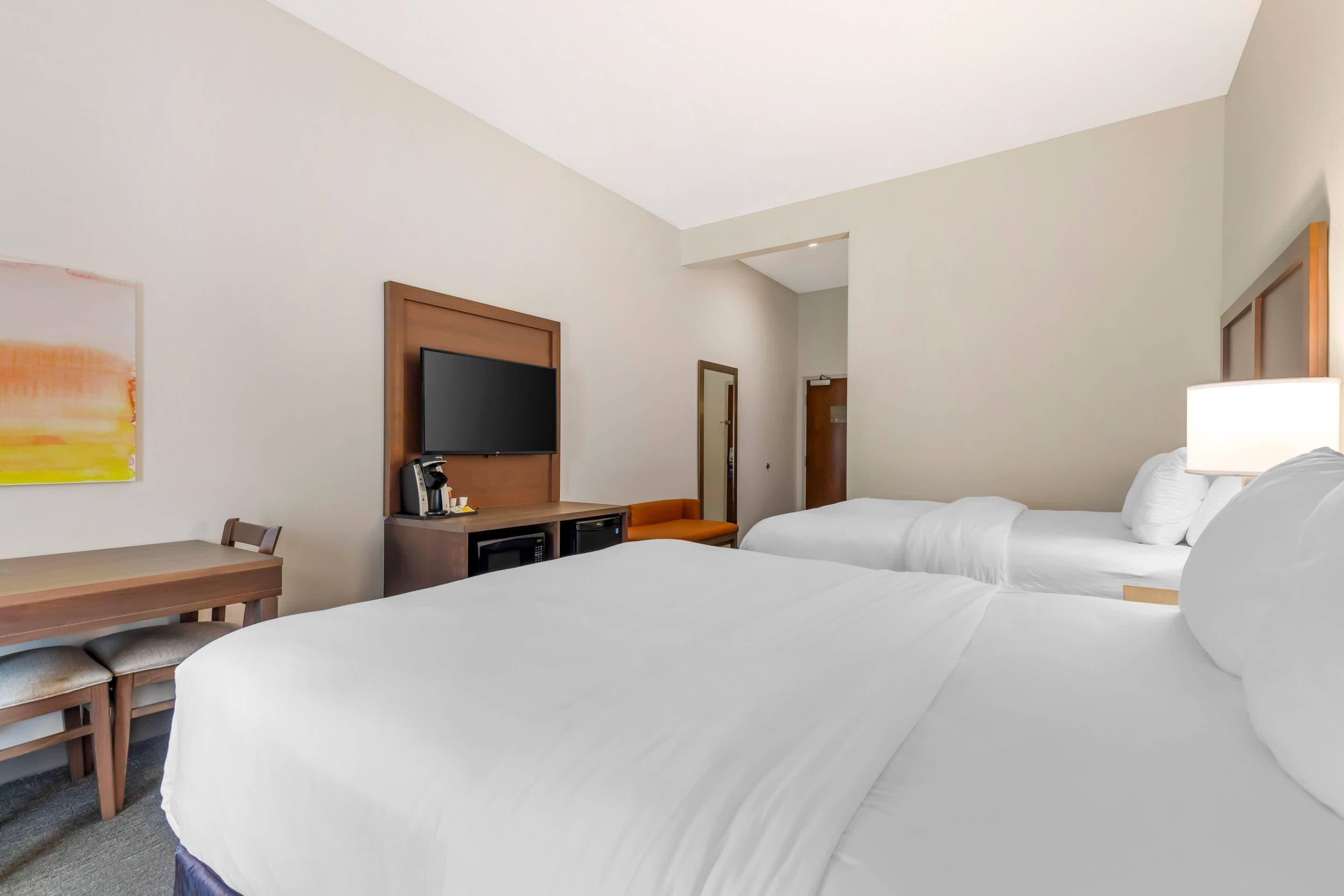 Una habitación de hotel con una cama grande, un escritorio con silla, un televisor y una cafetera.