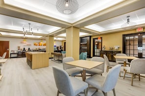 A spacious dining area with multiple tables and chairs, a central island, and a kitchen in the background.
