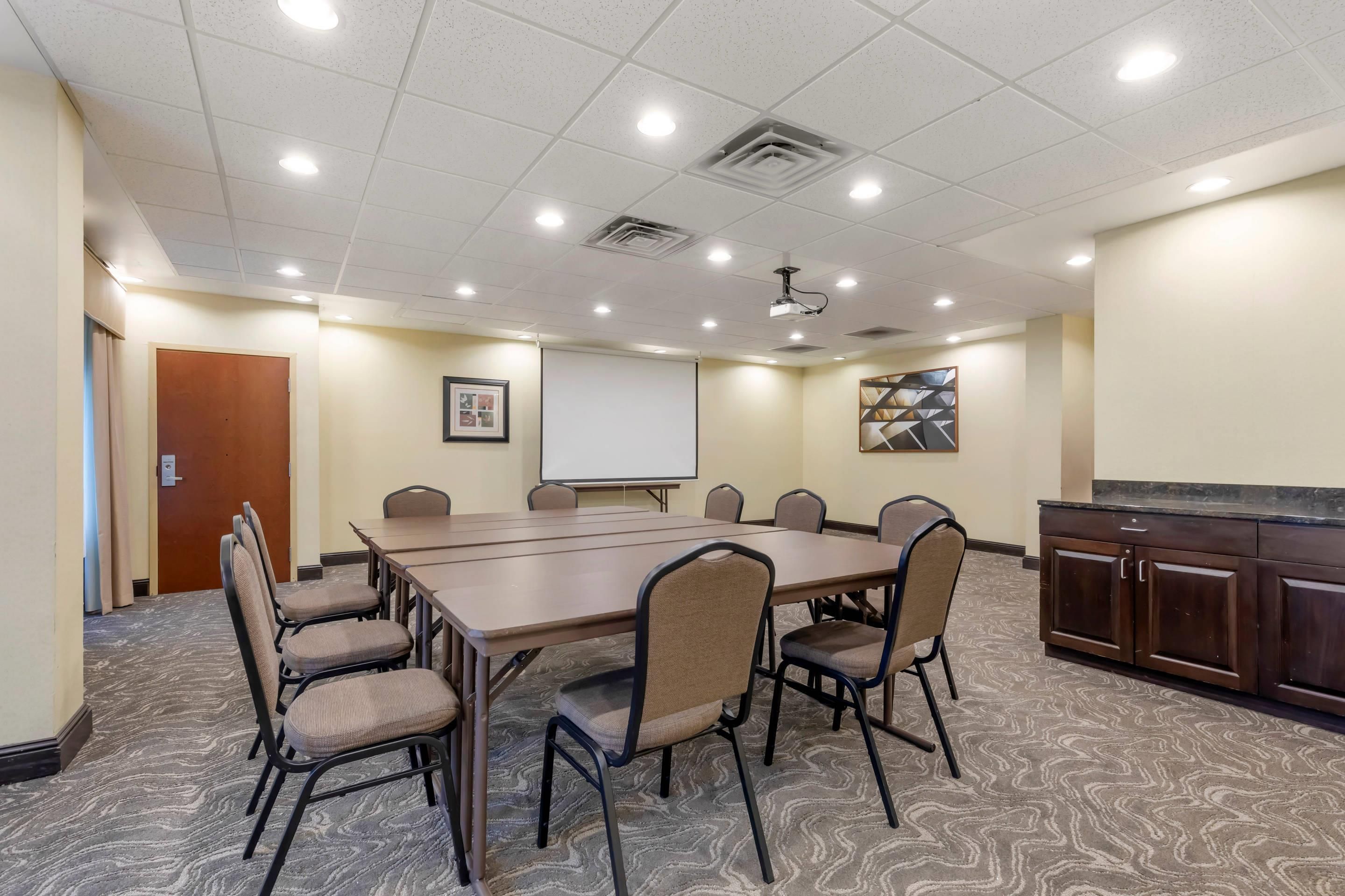 A conference room with a large table, chairs, a projector, a whiteboard, and a cabinet.