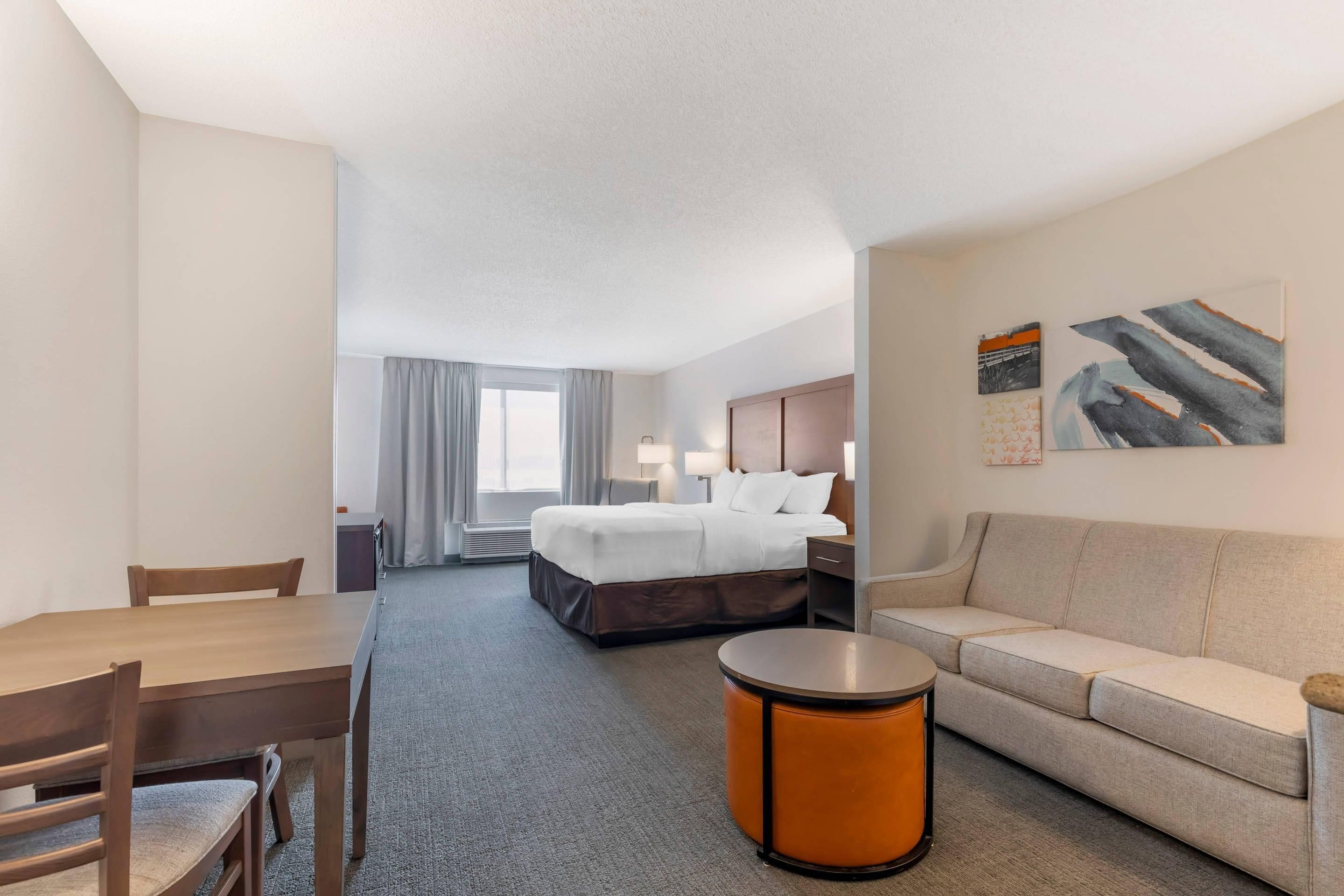 A hotel room with a bed, a sofa, a dining table, and a small round table.
