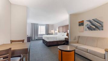 A hotel room with a bed, a sofa, a dining table, and a small round table.