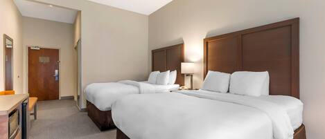 A hotel room with two beds, a desk, a chair, a lamp, and a door.