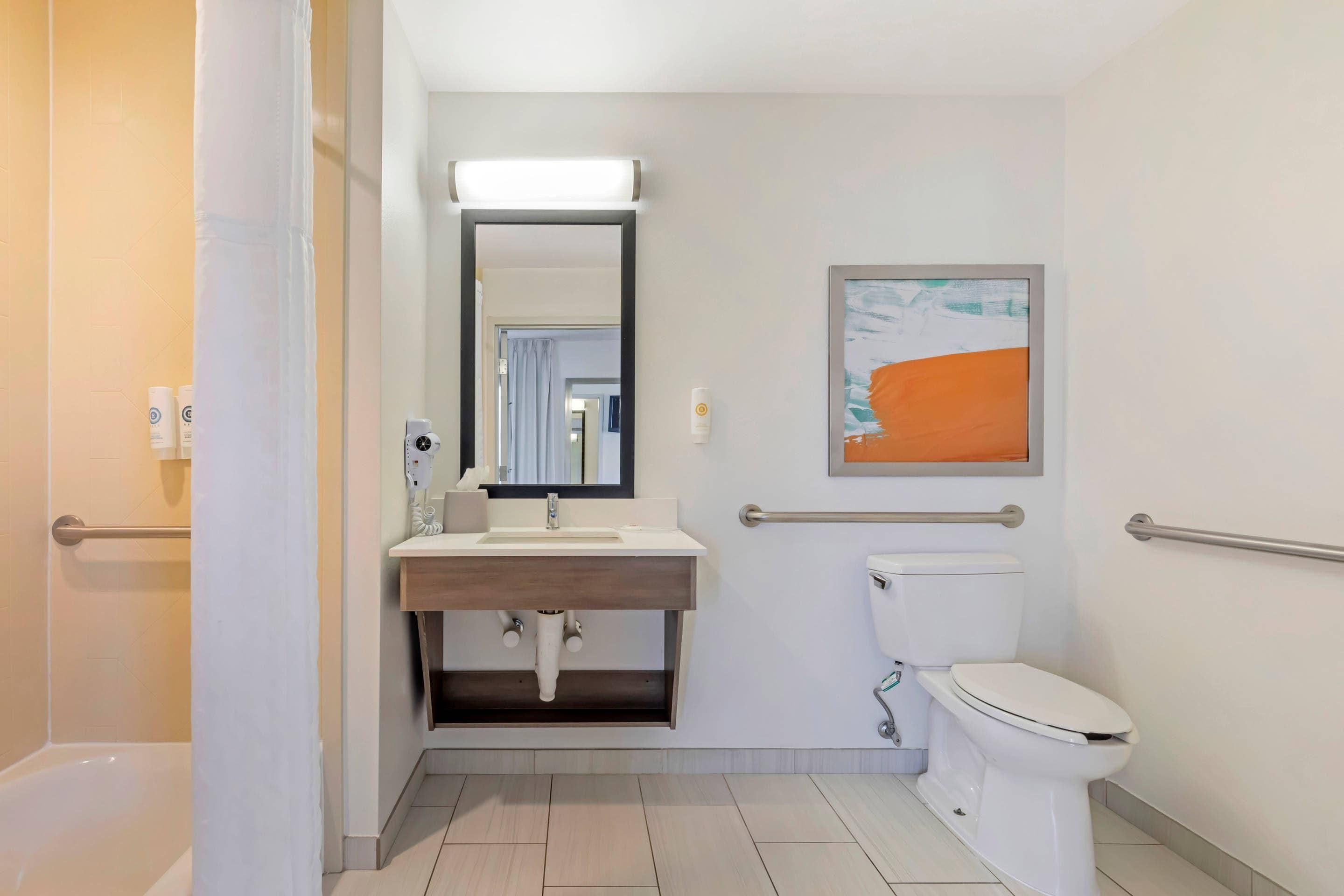 Une salle de bain moderne avec un lavabo blanc, un miroir et des toilettes. On y trouve également un sèche-mains et un porte-serviettes.