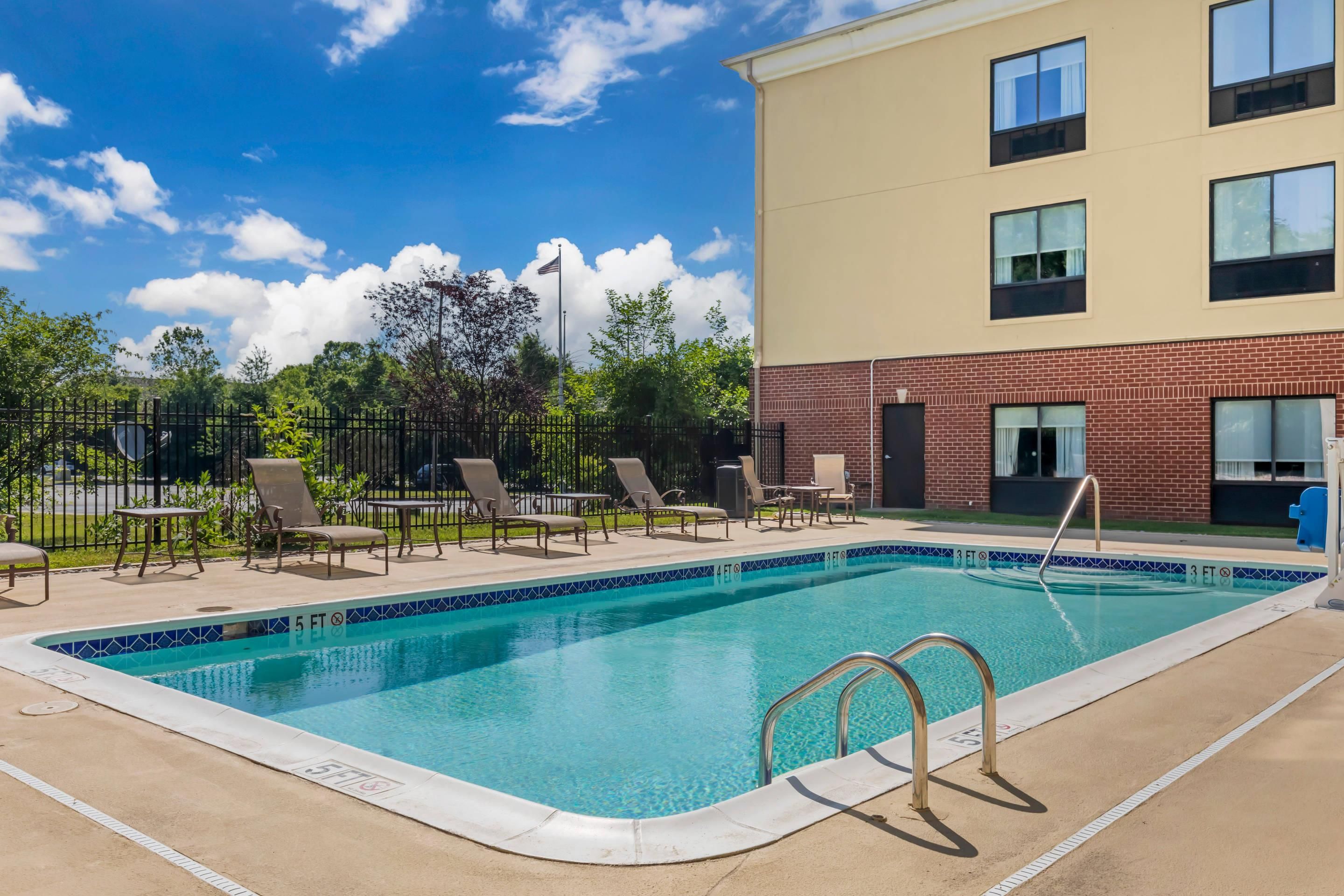 A swimming pool with lounge chairs and tables, surrounded by a fence and trees.