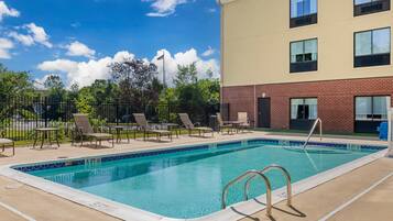 A swimming pool with lounge chairs and tables, surrounded by a fence and trees.