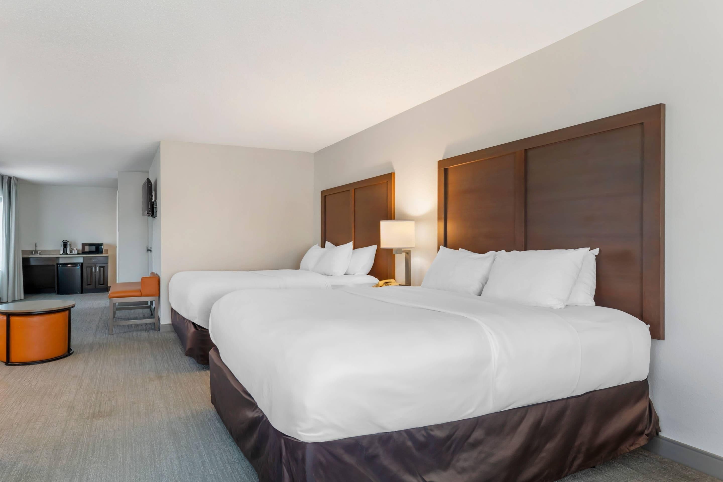 A hotel room with two beds, a desk, a chair, a lamp, and a small table.