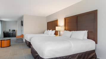 A hotel room with two beds, a desk, a chair, a lamp, and a small table.