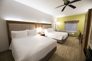 Une chambre d’hôtel avec deux lits, un ventilateur de plafond, une table de chevet avec une lampe et une fenêtre avec des rideaux.