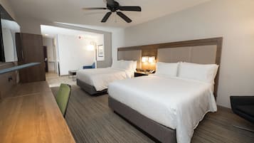 A hotel room with two beds, a desk, a chair, a ceiling fan, and a wooden floor.