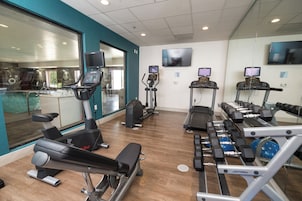 Academia com máquinas de cardio, bancos de peso e halteres.