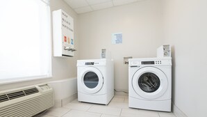 A laundry room with two front-loading washing machines, a wall-mounted air conditioner, and a sign indicating laundry products are available for purchase.