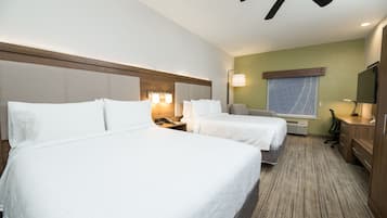Habitación de hotel con dos camas, ventilador de techo, televisor, escritorio con lámpara y ventana con vista.