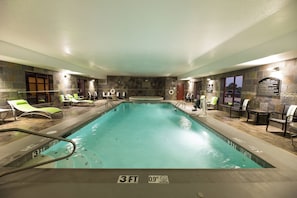 An indoor swimming pool with a 3 FT depth, surrounded by lounge chairs and a stone wall.