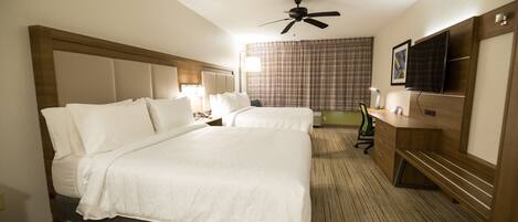 A hotel room with two beds, a ceiling fan, a desk with a chair, and a television.