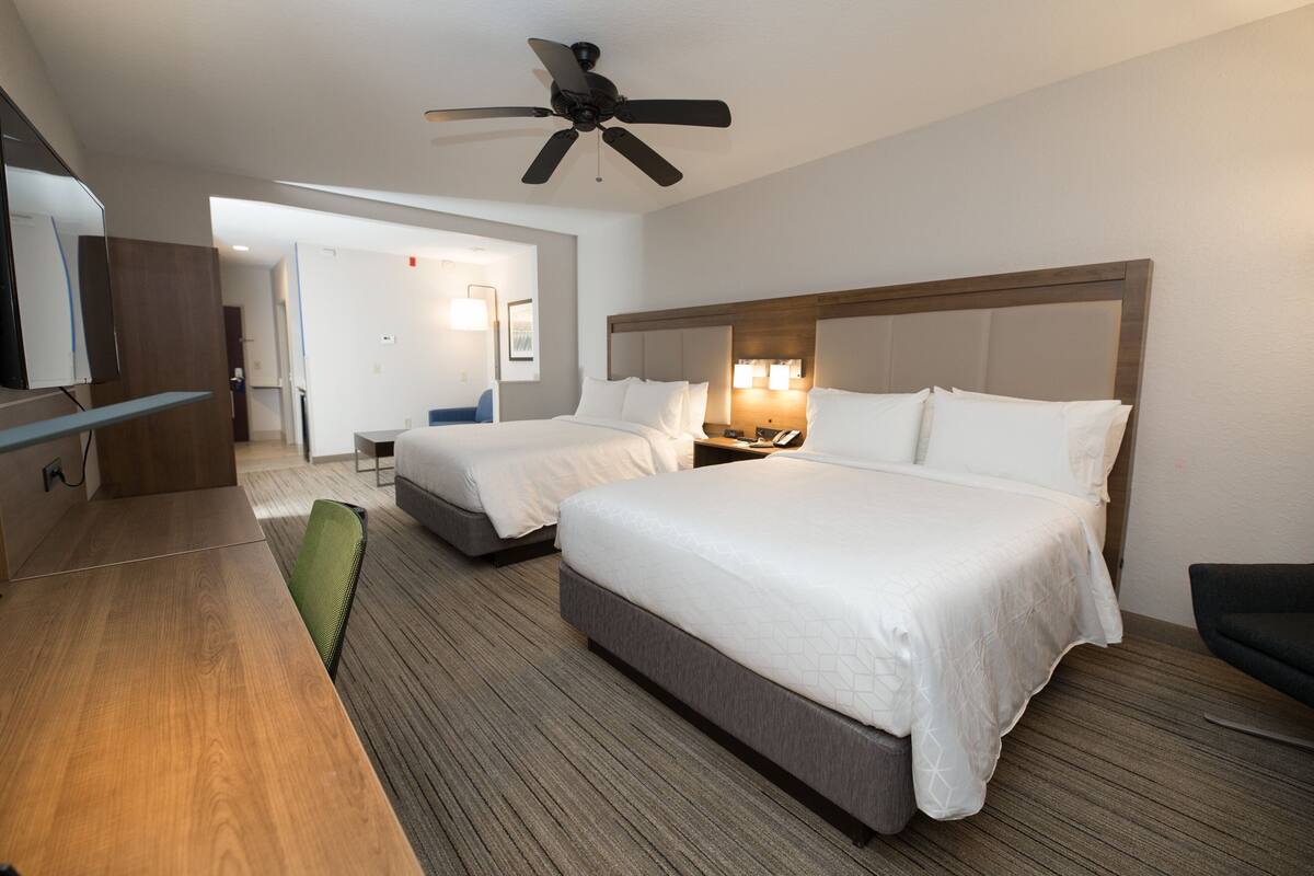A hotel room with two beds, a desk, a chair, a ceiling fan, and a TV.