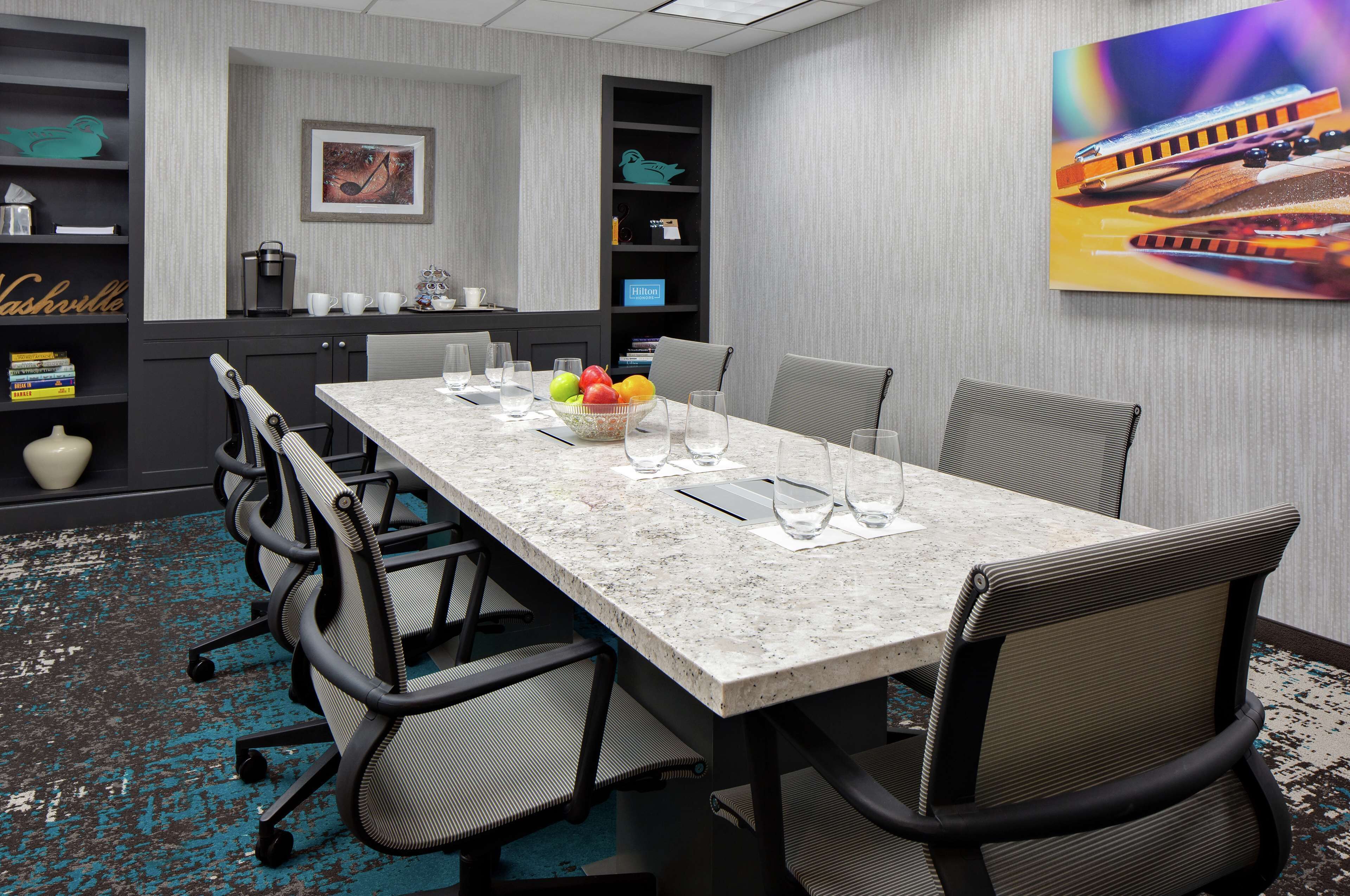 A conference room with a long table, chairs, a coffee station, and a bookshelf with a framed picture.