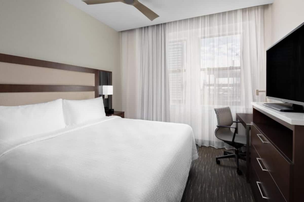 A hotel room with a large bed, a desk with a chair, a television, and a window with curtains.
