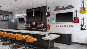 A modern bar area with a long counter, multiple stools, and guitars on the wall. - Homewood Suites by Hilton Nashville-Downtown (Nashville)