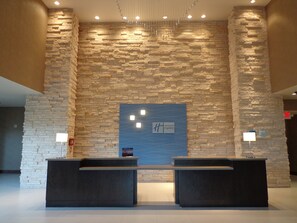 Ett välkomstområde med en vägg av sten som bakgrund, två receptionsdiskar och en blå skylt med Holiday Inn Express-logotypen.