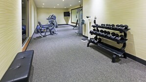 A gym with exercise equipment, a bench, and a rack of dumbbells.