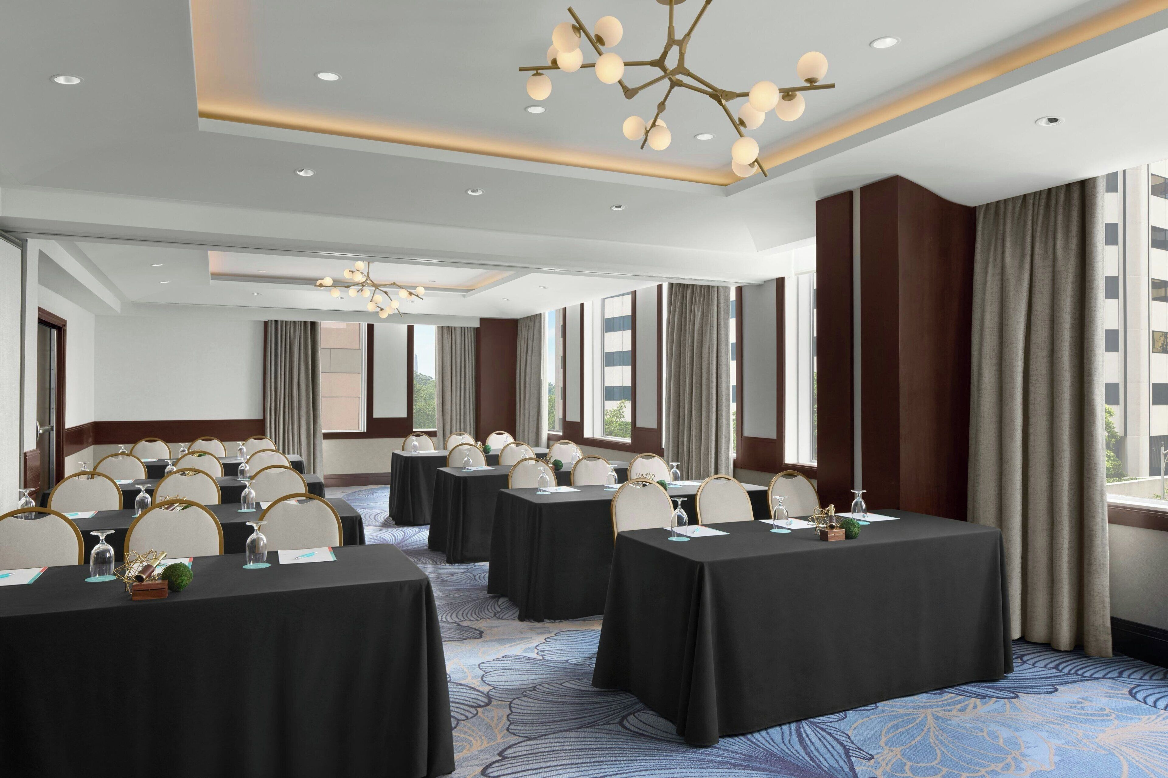 Un salón de conferencias con varias mesas, sillas y una lámpara de araña moderna.