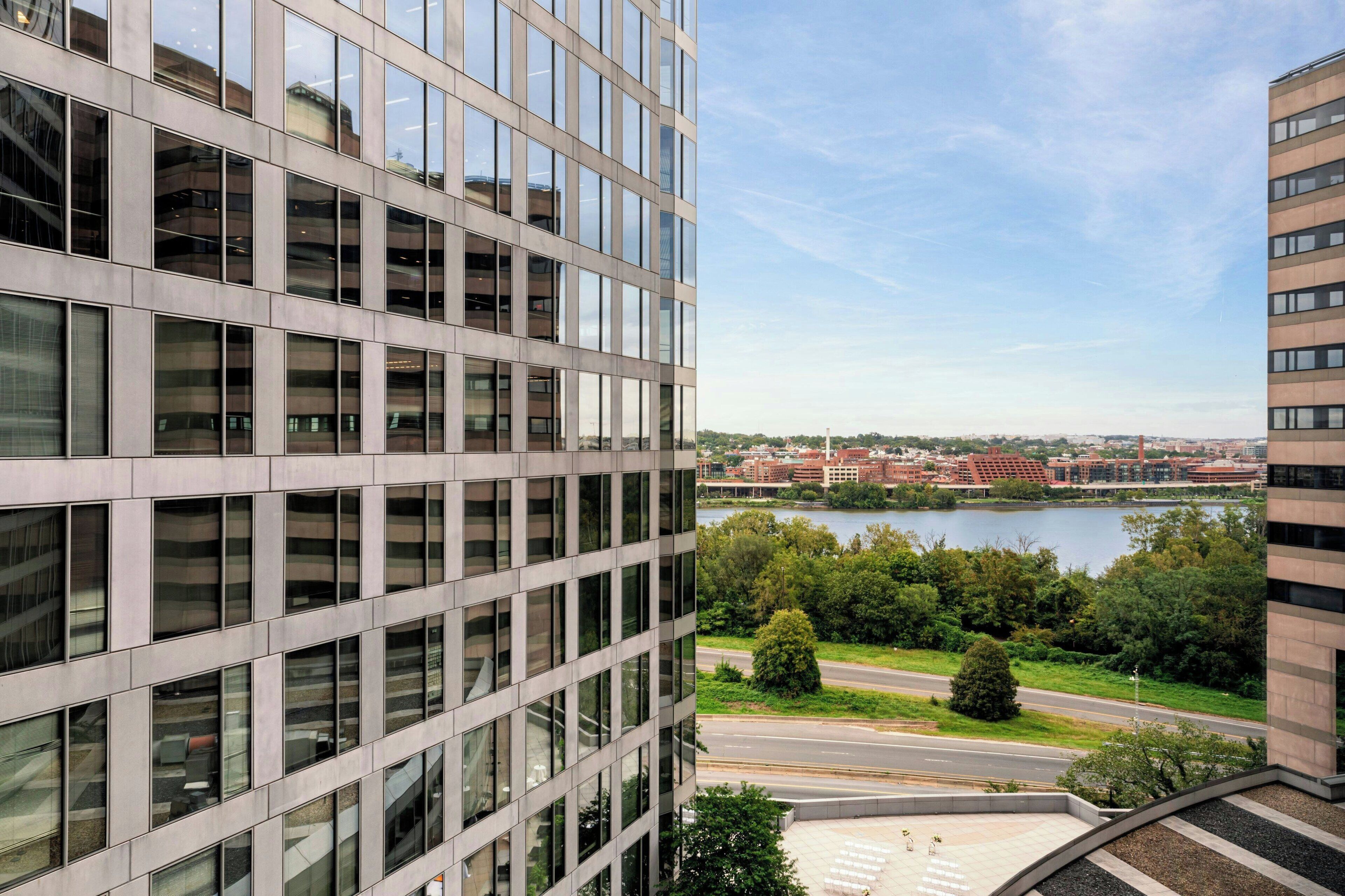 A modern building with a glass facade overlooking a river and a cityscape.