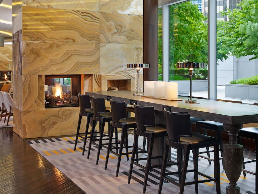 A modern bar area with a marble wall, bar stools, and a large window offering a view of greenery outside.