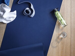 Een blauwe yogamat, een witte handdoek, een opgerolde yogariem, een waterfles met komkommerplakjes en een glas water op een houten ondergrond.