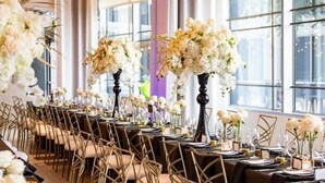 A long banquet table with white floral centerpieces, gold chairs, and a modern interior with large windows. - Le Meridien Arlington (Arlington)