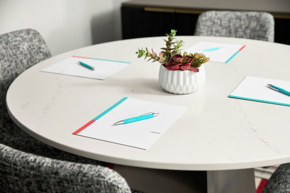 A round table with a white surface, surrounded by grey upholstered chairs. A small white vase with a succulent plant is placed in the center.
