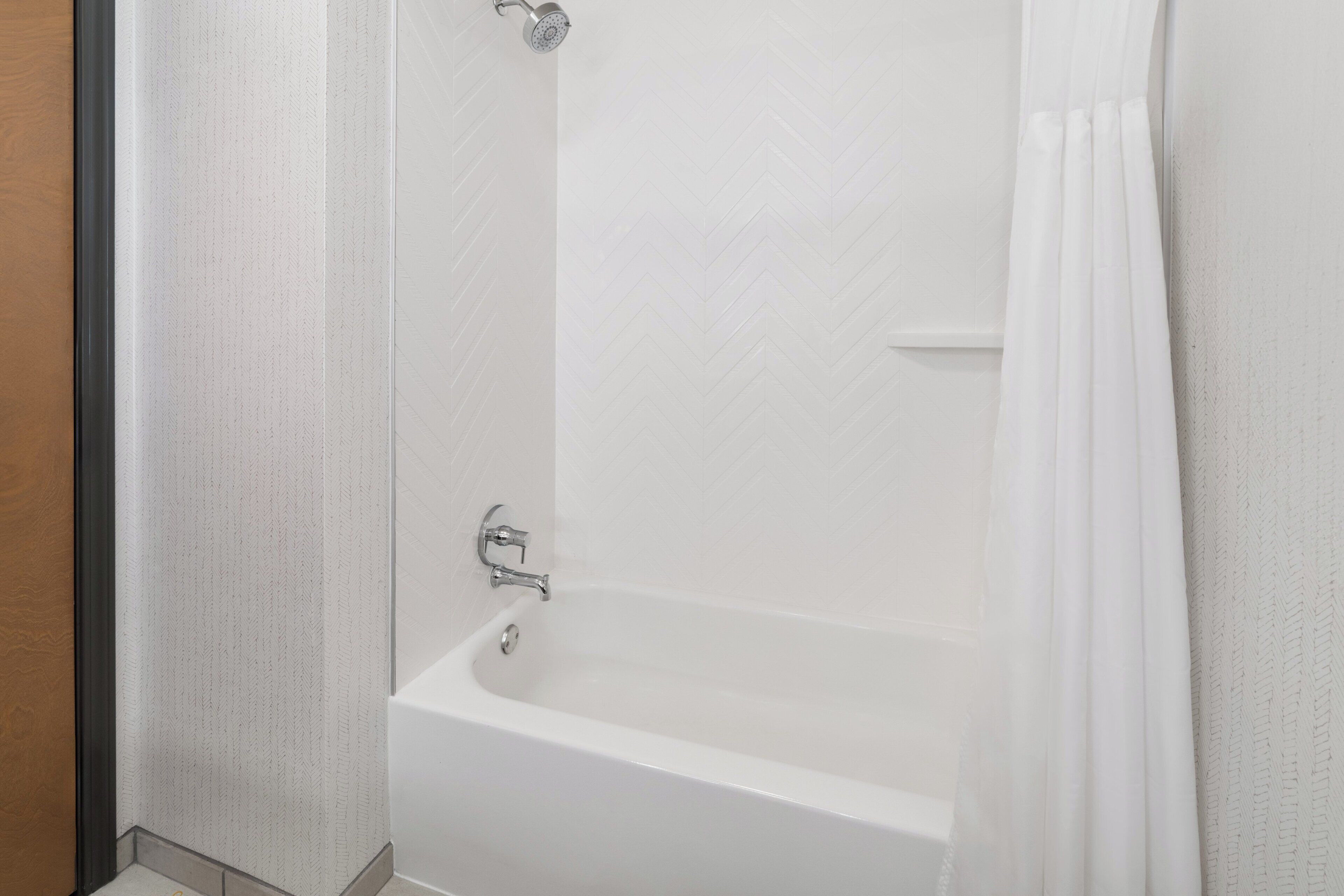 A white bathtub with a showerhead, a curtain, and a wall with a herringbone pattern.