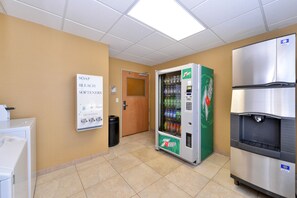 A restroom with a 7Up vending machine, a refrigerator, and a soap and bleach dispenser.