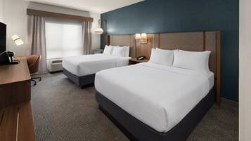 A hotel room with two beds, a desk, a chair, a TV, and a window with curtains.