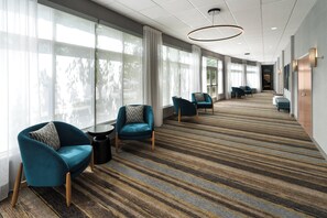 A hotel lobby with a carpeted floor, seating area with chairs, large windows, and a reception desk. - Holiday Inn Laramie by IHG (Laramie)
