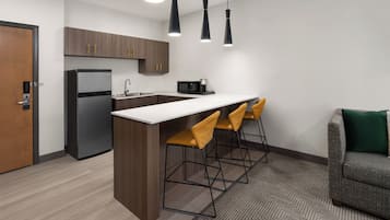 Een moderne keuken met een koelkast, magnetron en barstoelen.