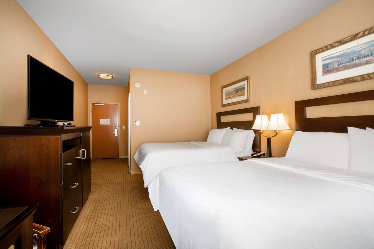A hotel room with two beds, a TV, a desk, and a lamp.