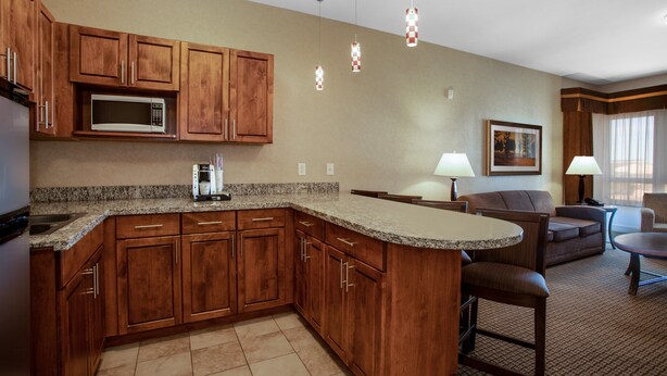 A kitchen with wooden cabinets, a microwave, and a granite countertop. There is a dining area with a table and chairs. - Holiday Inn Laramie by IHG (Laramie)