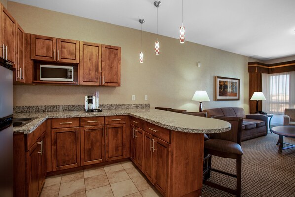 A kitchen with wooden cabinets, a microwave, and a granite countertop. There is a dining area with a table and chairs.