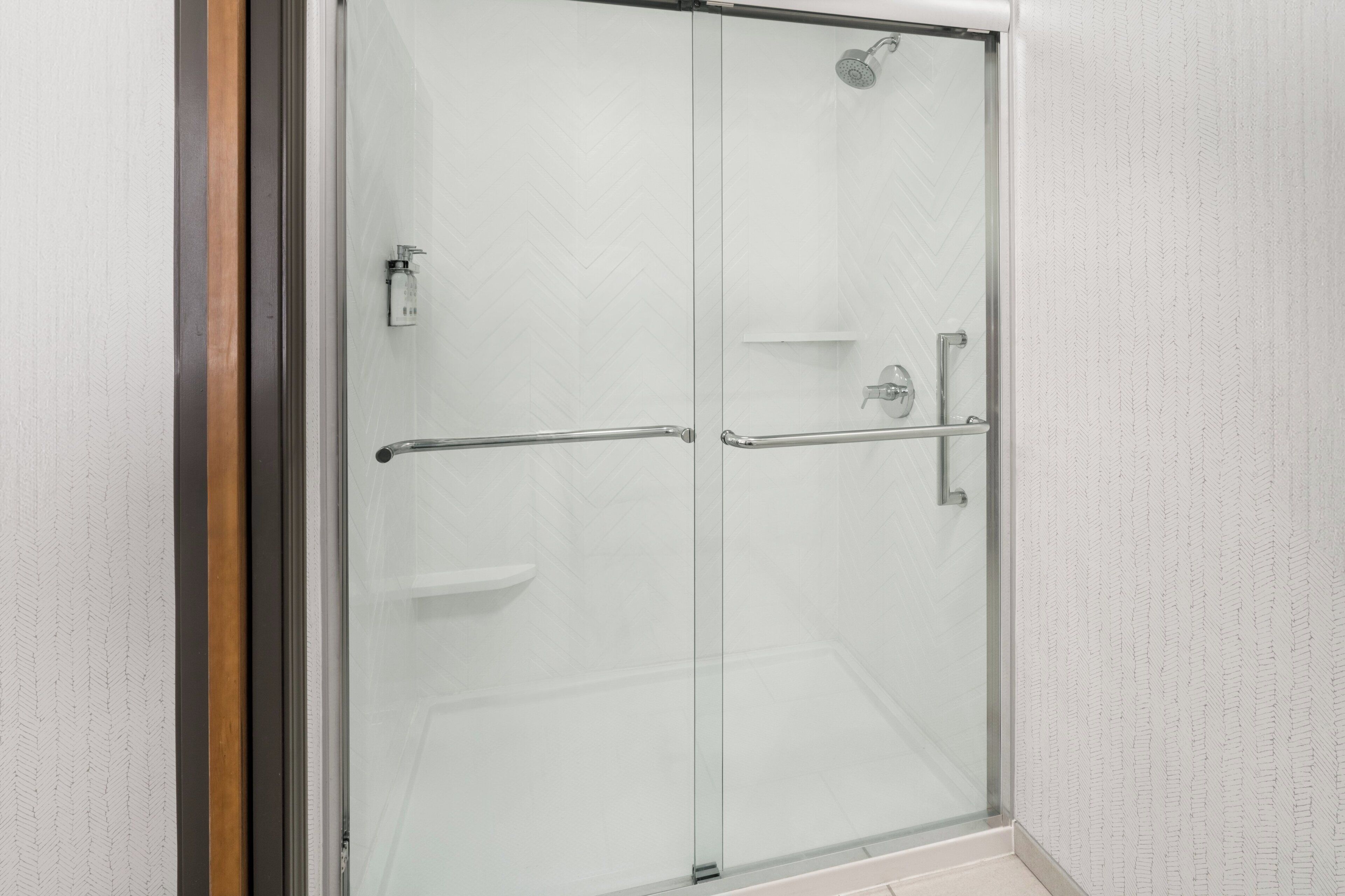 Une cabine de douche fermée par des parois en verre, équipée d’une barre d’appui et d’un pommeau de douche.