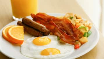 Un plato con huevos, tocino, salchichas y patatas ralladas.