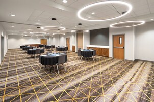 Un salón de conferencias con mesas redondas, sillas y piso alfombrado.