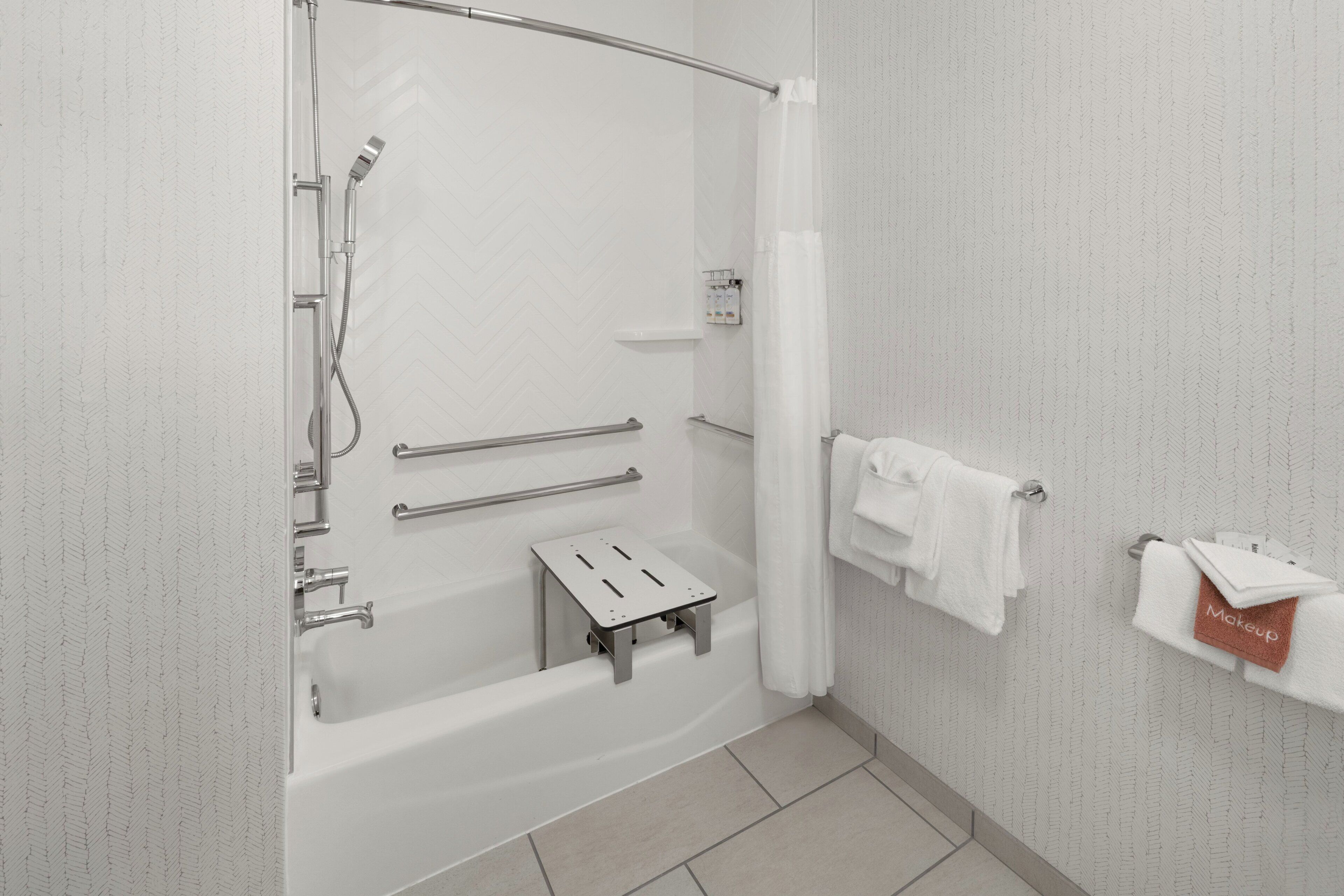A modern bathroom with a bathtub, shower, grab bars, a towel rack, and a small step stool.