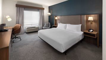 Ein Hotelzimmer mit einem großen Bett, einem Schreibtisch, einem Stuhl, einer Schreibtischlampe, einem Telefon und einem Fenster mit Vorhängen.