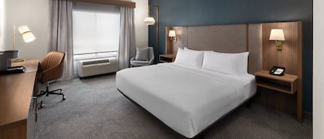 Habitación de hotel con una cama grande, un escritorio, una silla, una lámpara de escritorio, un teléfono y una ventana con cortinas.