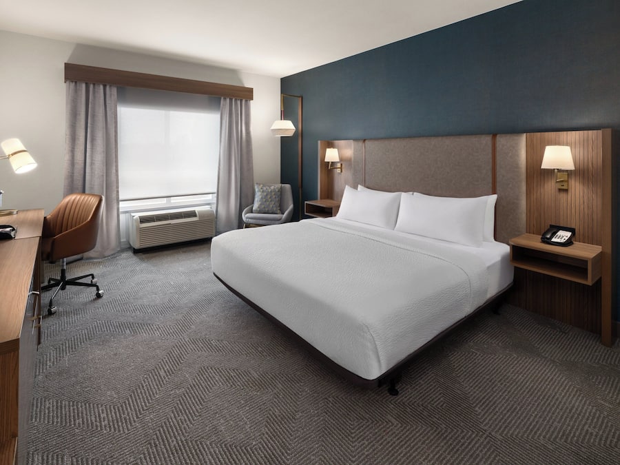 Hotelkamer met groot bed, bureau, stoel, bureaulamp, telefoon en raam met gordijnen.