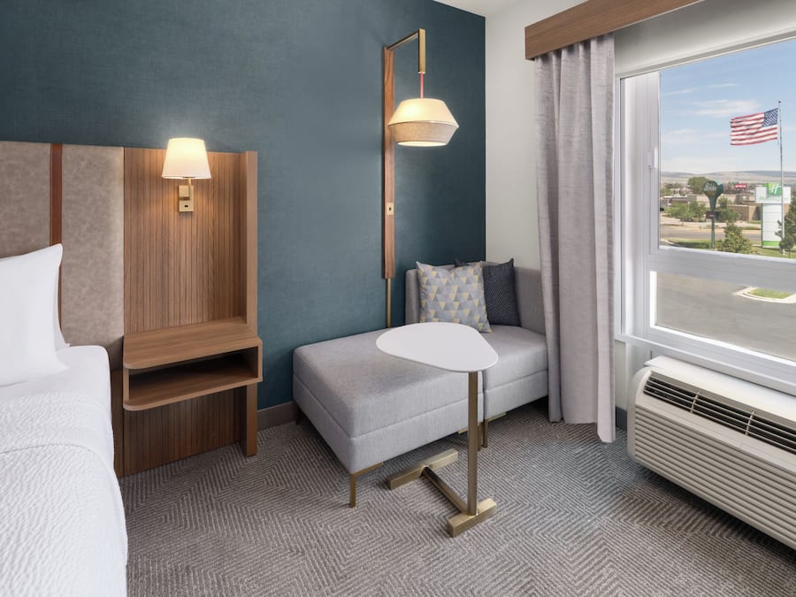 A hotel room with a bed, a small table, a sofa, a lamp, and a window with an American flag.