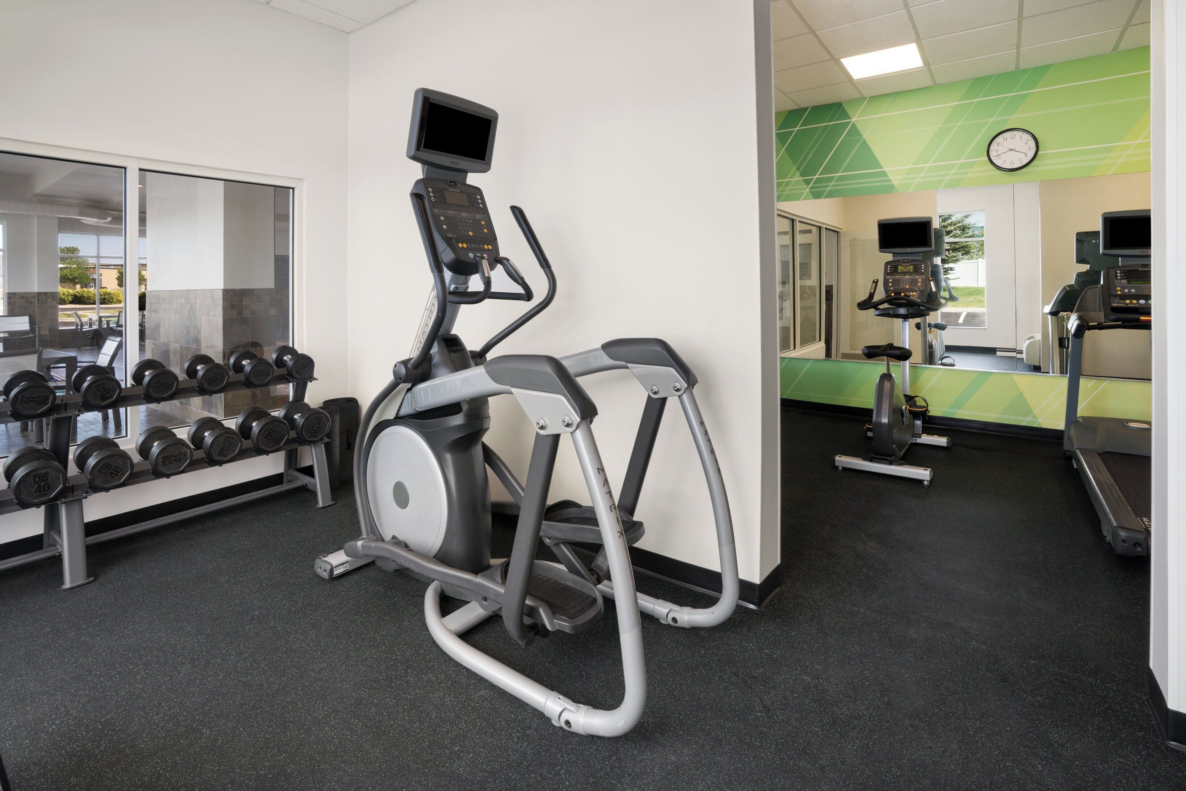 A gym with exercise equipment including an elliptical, treadmills, and dumbbells.