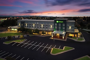 A Holiday Inn hotel with a parking lot and a sunset in the background. - Holiday Inn Laramie by IHG (Laramie)
